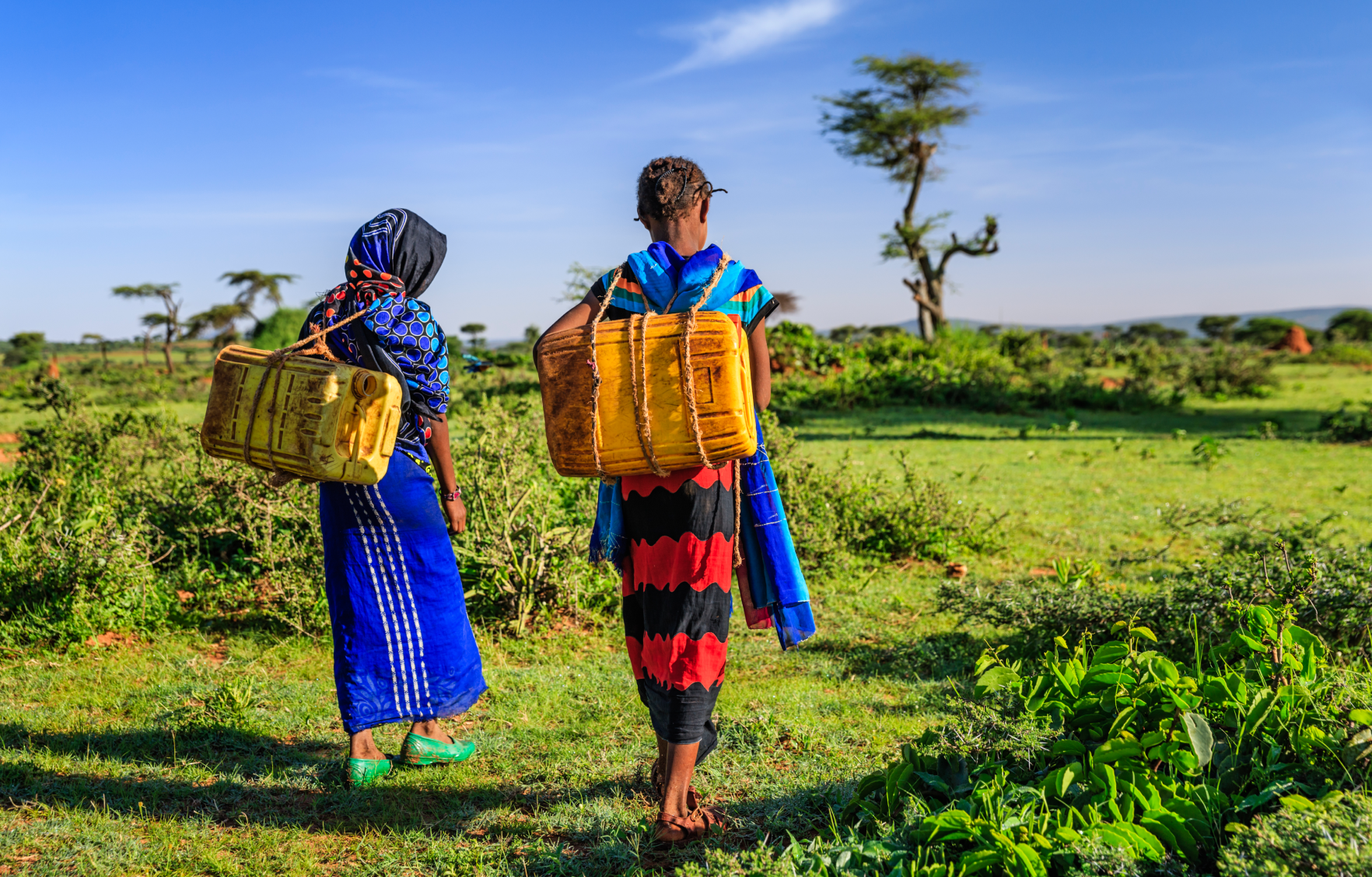 Two women walking in field with a bag