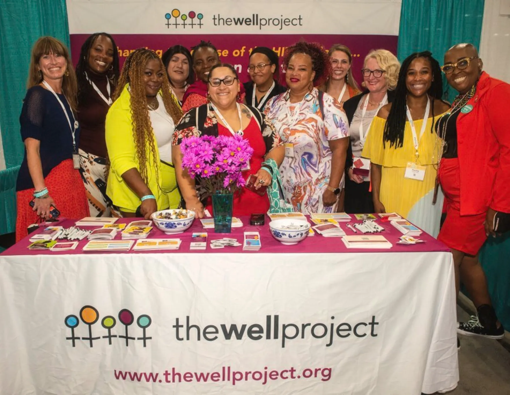 A group of people standing behind a table as part of The Well Project, smiling