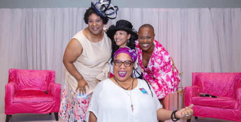 Four women smiling in front of bright pink chairs