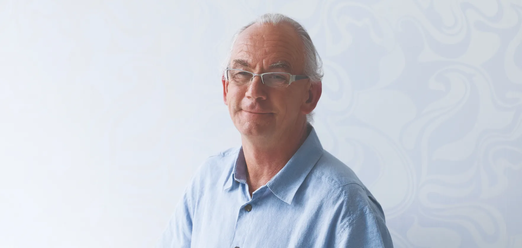 A smiling man wearing a blue shirt and glasses