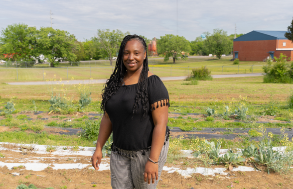 A woman standing and smiling with a country background