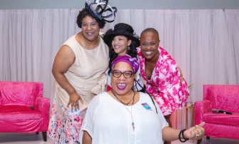 Four women smiling in front of bright pink chairs